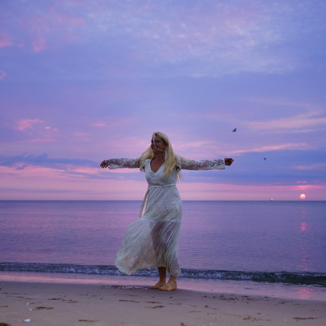Annett Punte tanzt am Strand bei rosa Sonnenuntergang
